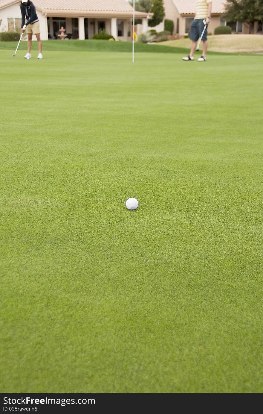 A golf ball on the green of a golf course with golfers in the background.