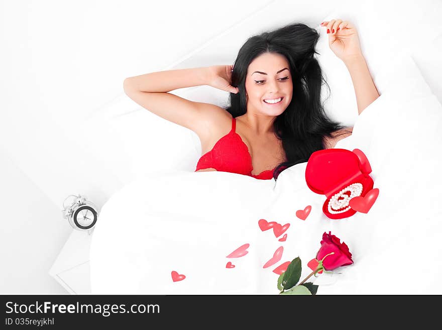 Beautiful brunette woman waking up at home on a Valentine's day with presents and a rose near her, prepared by her husband