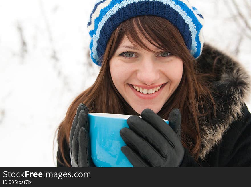 Beautiful girl in a striped beret laughing and holding a large blue mug. Beautiful girl in a striped beret laughing and holding a large blue mug