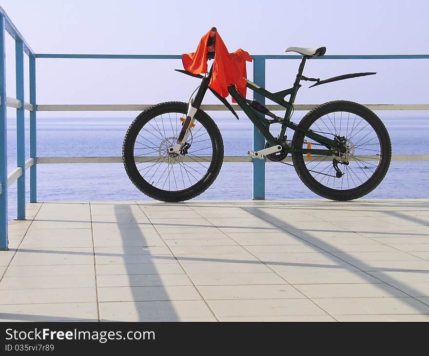 Alone bicycle at the seafront fence in sunny day against blue sea and sky