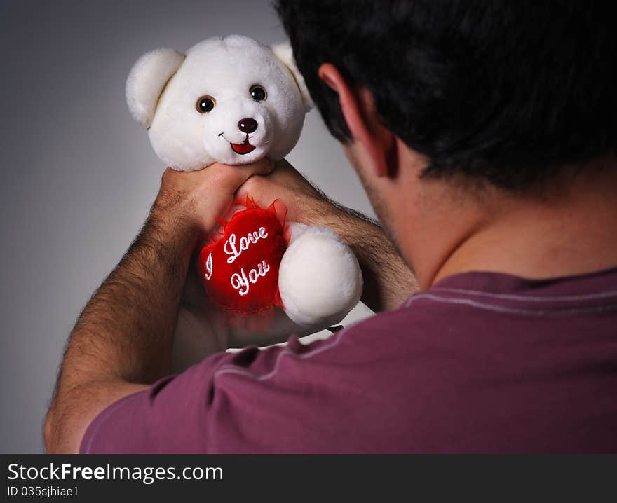 Frustrated man strangling a valentine teddy bear. Frustrated man strangling a valentine teddy bear