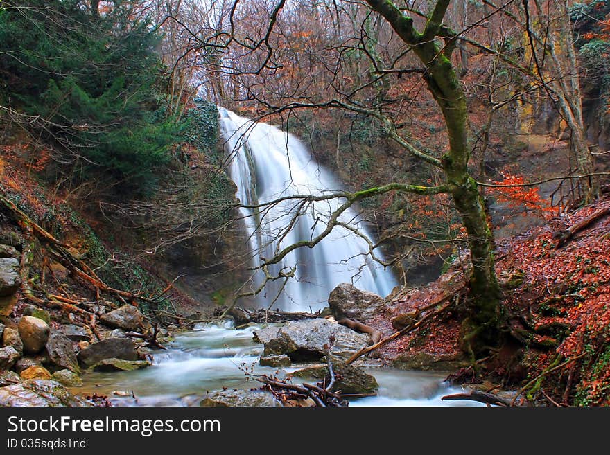 Trees in autumn colors around a waterfall with the flow of the cascading water smoothed by slow shutter speed. Trees in autumn colors around a waterfall with the flow of the cascading water smoothed by slow shutter speed.