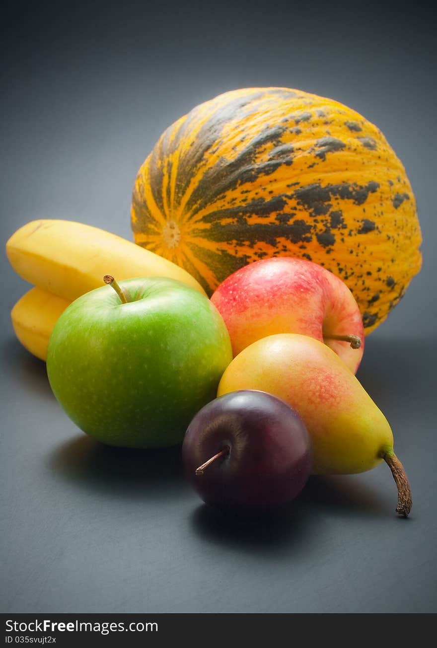 Fresh, ripe colorful fruits - plum, pear, apples, bananas and melon arranged on dark background