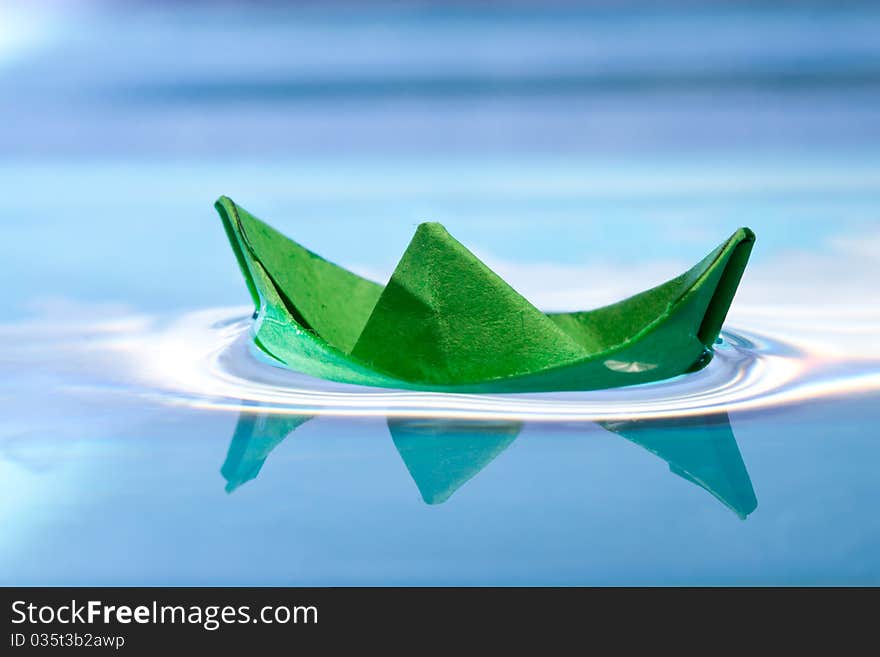 Green paper boat with reflection on blue water. Green paper boat with reflection on blue water