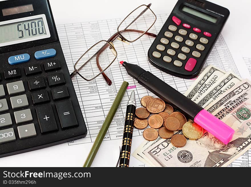 Calculator, glasses, pen, dollars and coins on the background papers to the amounts. Calculator, glasses, pen, dollars and coins on the background papers to the amounts