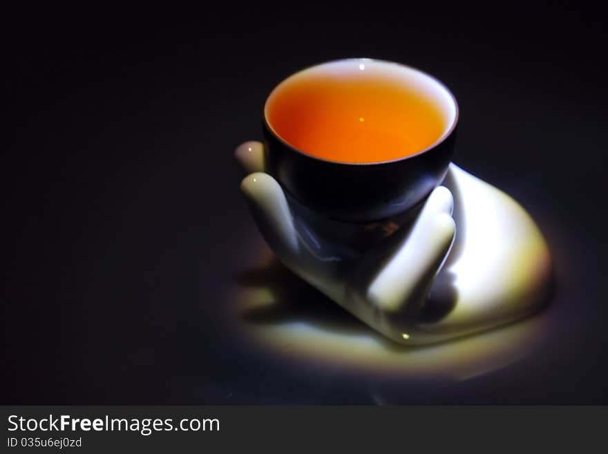 A teacup with tea on a hand-shape sculpture with black background.