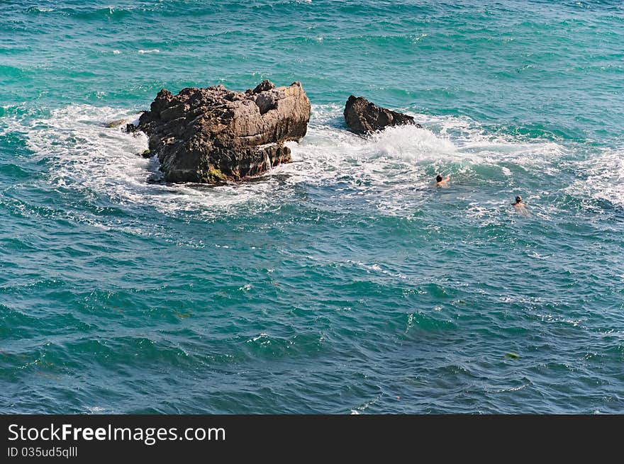 Men swim in the blue sea near rocks. Men swim in the blue sea near rocks