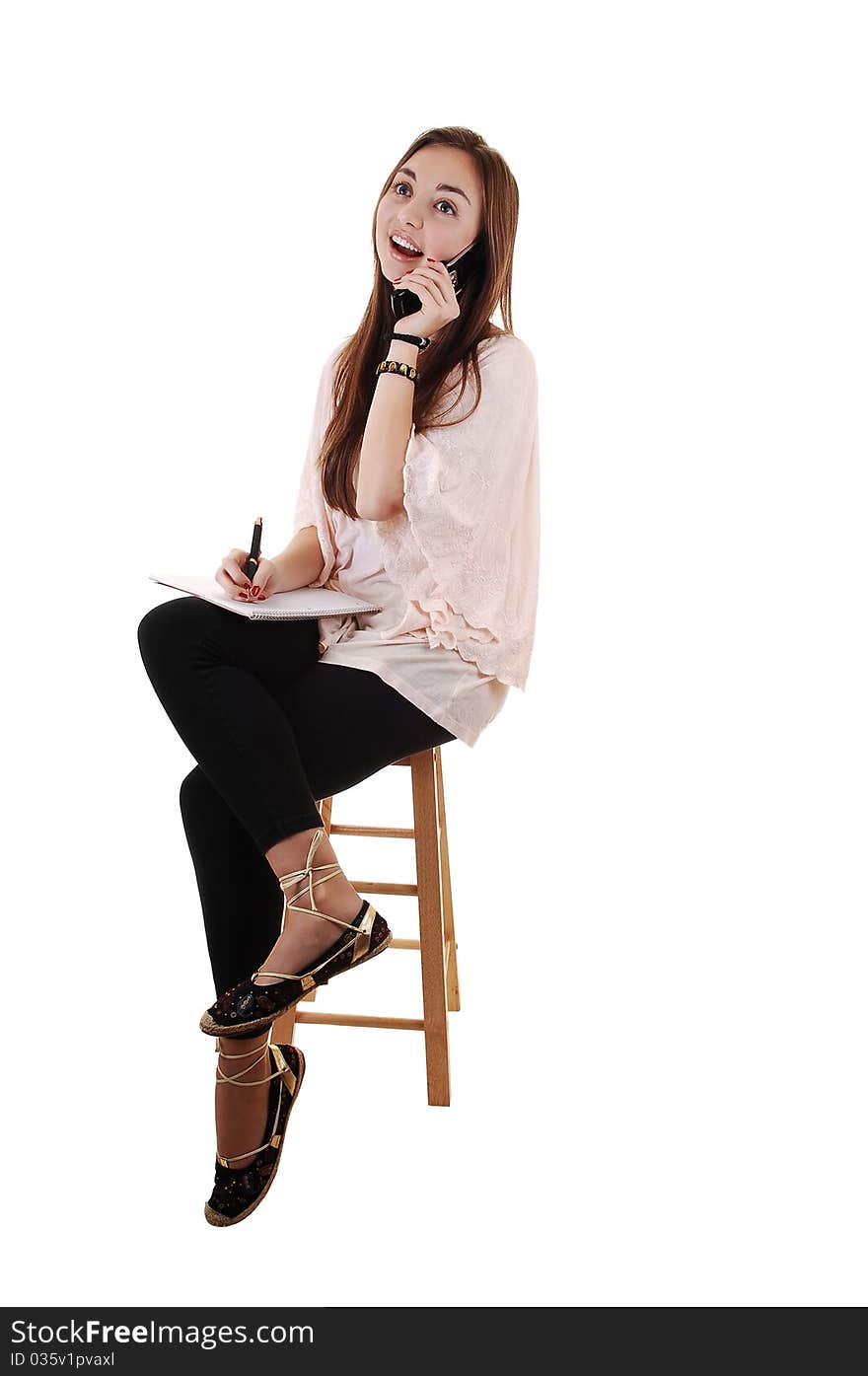 A young teenager sitting on a chair, in black tights and with long brunette hair and a notebook in her hand, on the cell phone, for white background. A young teenager sitting on a chair, in black tights and with long brunette hair and a notebook in her hand, on the cell phone, for white background.