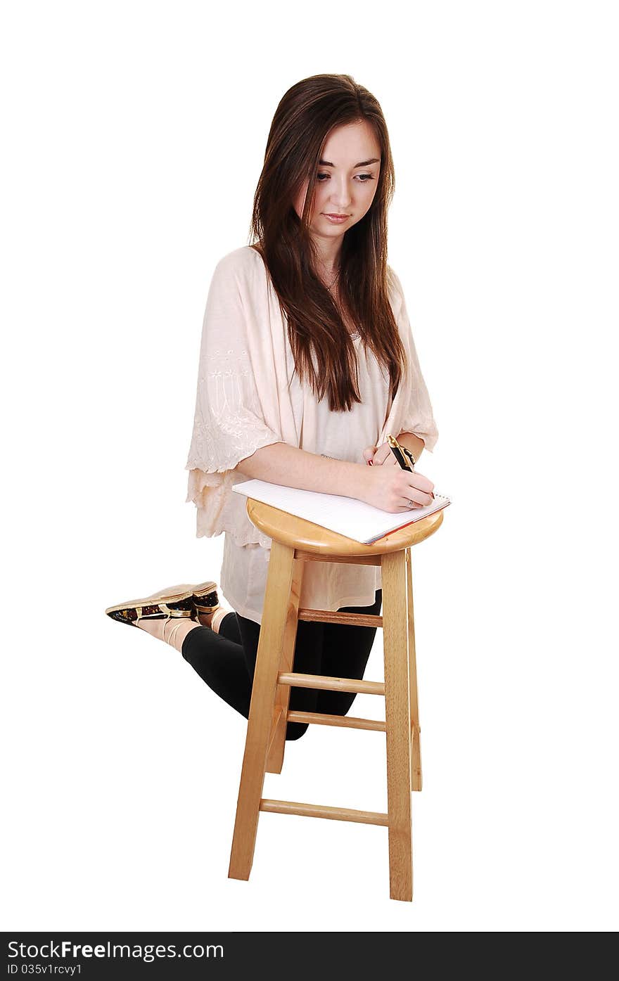 A young teenager kneeling on the floore, in tights and with long brunette hair and a notebook on a chair in front of her, for white background. A young teenager kneeling on the floore, in tights and with long brunette hair and a notebook on a chair in front of her, for white background.