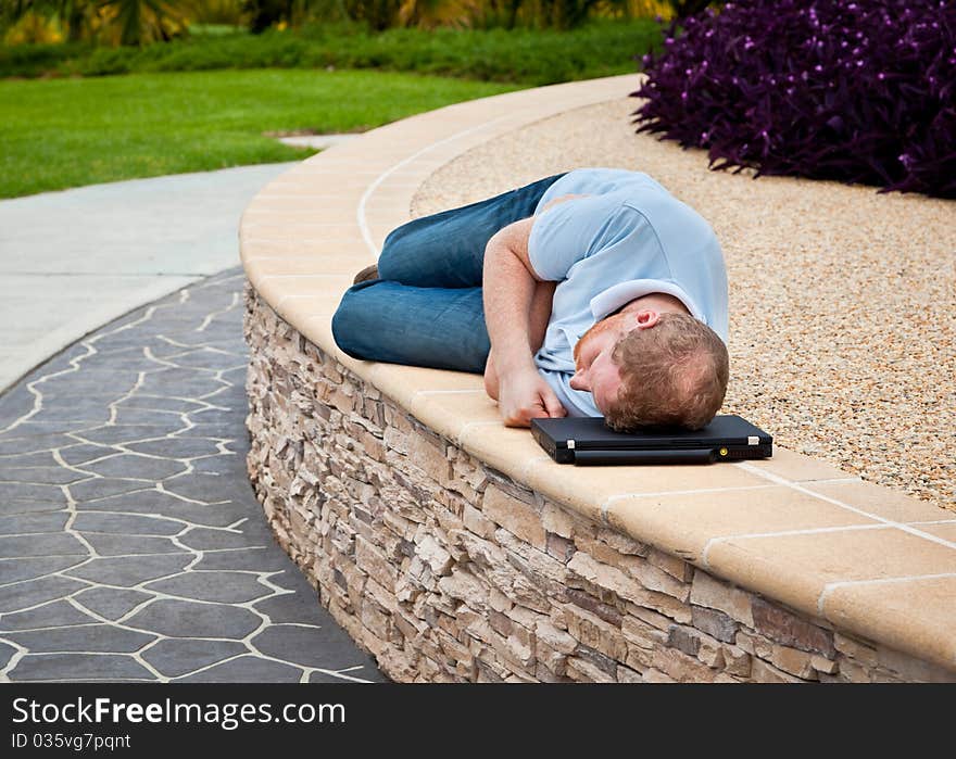 Man sleeping on a wall in a park using a laptop computer as his pillow. Man sleeping on a wall in a park using a laptop computer as his pillow.