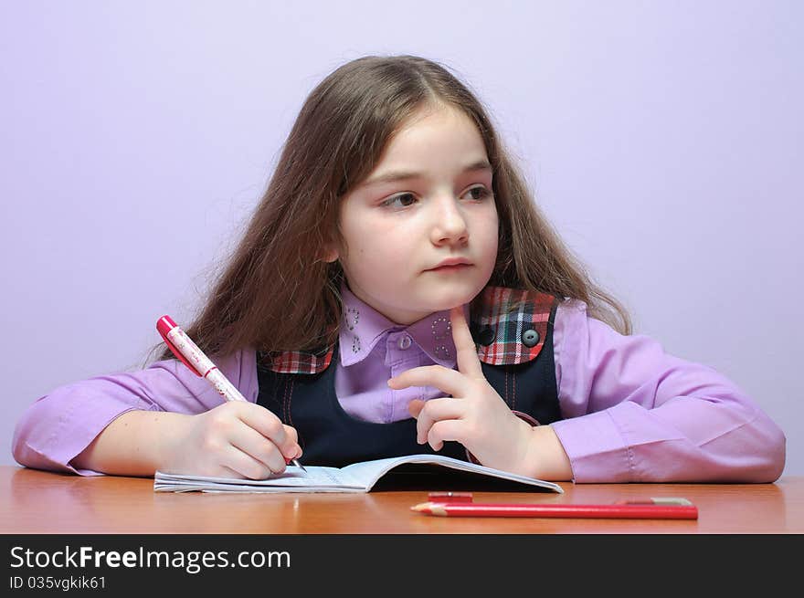 Portrait of a little school girl doing homeworks at desk and thinking.