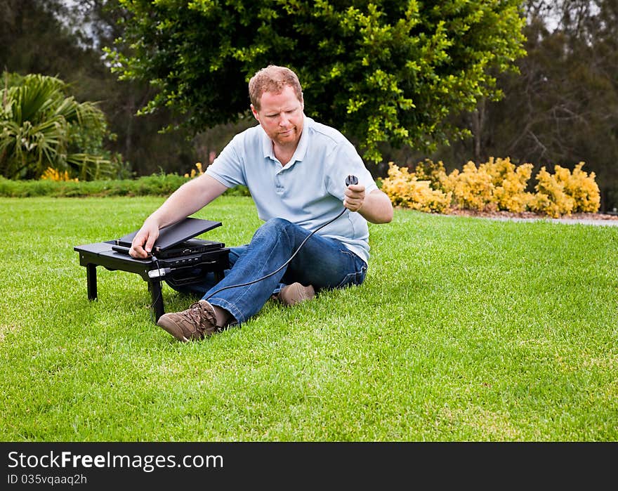 Man using laptop computer in a park and wondering where to plug the power into. Man using laptop computer in a park and wondering where to plug the power into.