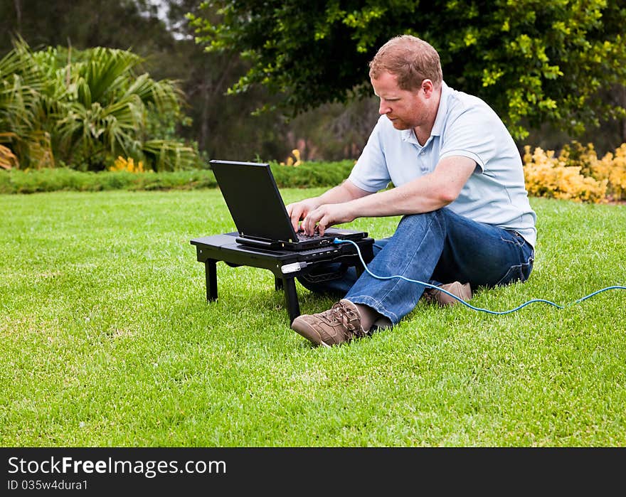 Man sitting cross legged on grass using a laptop computer connected with ethernet cable. Man sitting cross legged on grass using a laptop computer connected with ethernet cable.