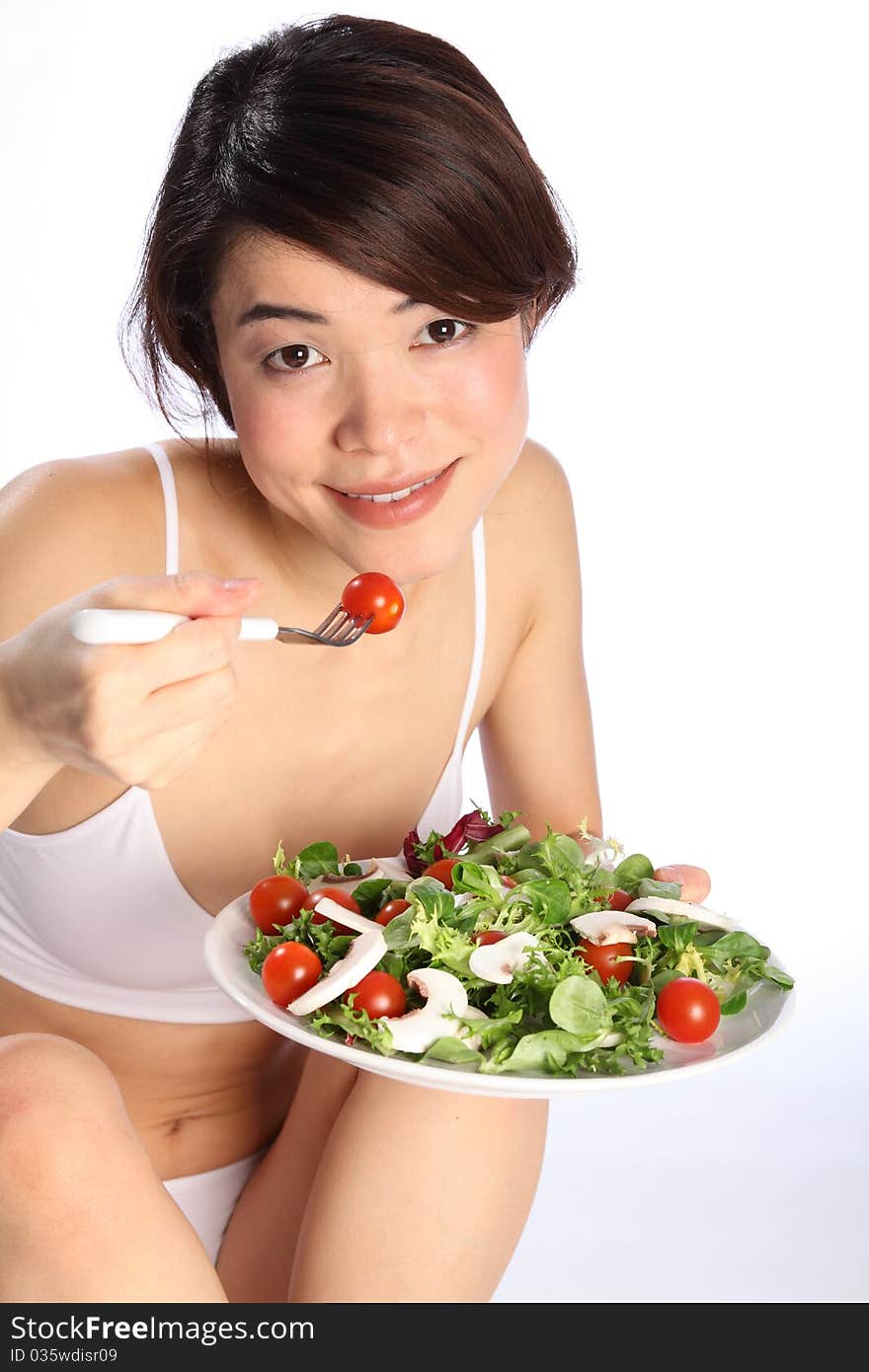 Beautiful, smiling young oriental girl, sitting on floor wearing sports underwear, showing off a healthy body while eating a salad. Beautiful, smiling young oriental girl, sitting on floor wearing sports underwear, showing off a healthy body while eating a salad.