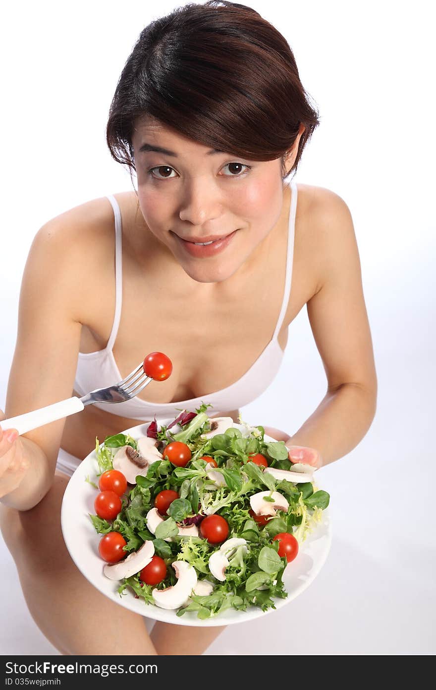 Beautiful, smiling young Japanese girl, wearing white sports bra, showing off a healthy body while eating a green salad. Beautiful, smiling young Japanese girl, wearing white sports bra, showing off a healthy body while eating a green salad.