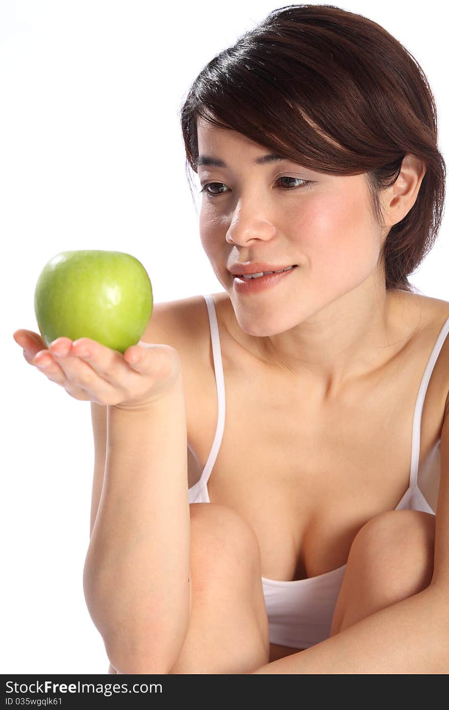 Beautiful young Japanese girl, wearing white sports underwear, sitting down holding a green apple. Beautiful young Japanese girl, wearing white sports underwear, sitting down holding a green apple.