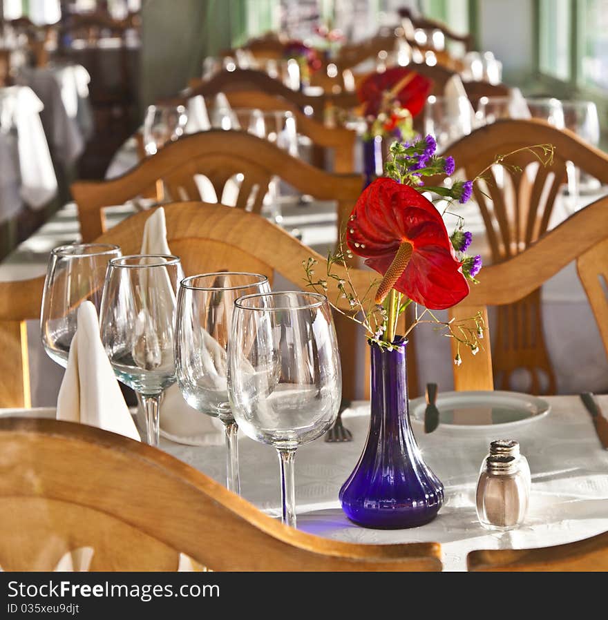 Table is set in a restaurant with glasses, flowers and tablecloth