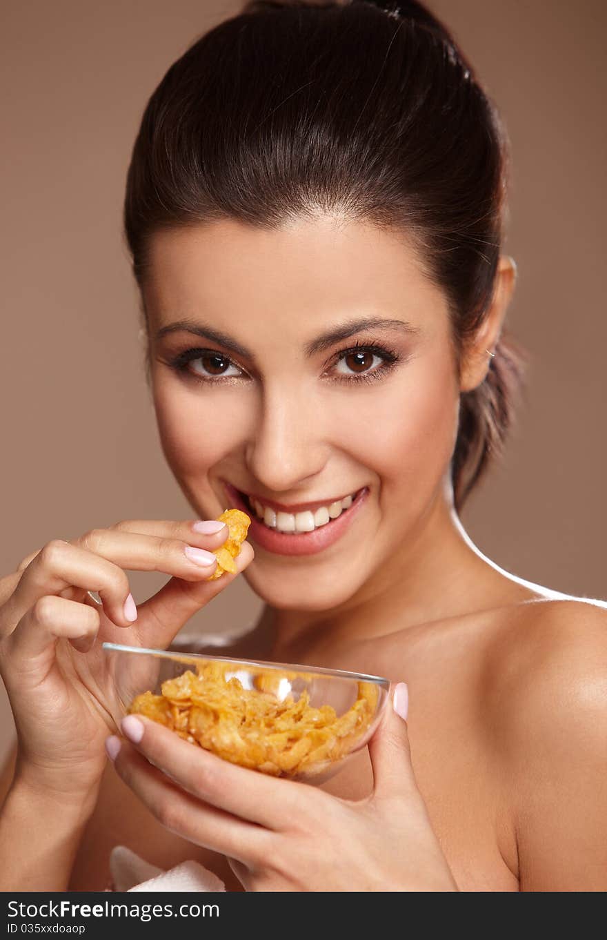 Portrait of a beautiful young woman eating cornflakes, isolated on beige. Portrait of a beautiful young woman eating cornflakes, isolated on beige