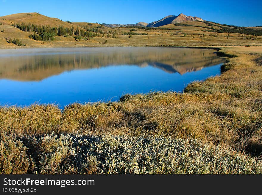 Steep mountain reflected in calm water of a blue lake surrounded by fall grass. Steep mountain reflected in calm water of a blue lake surrounded by fall grass.