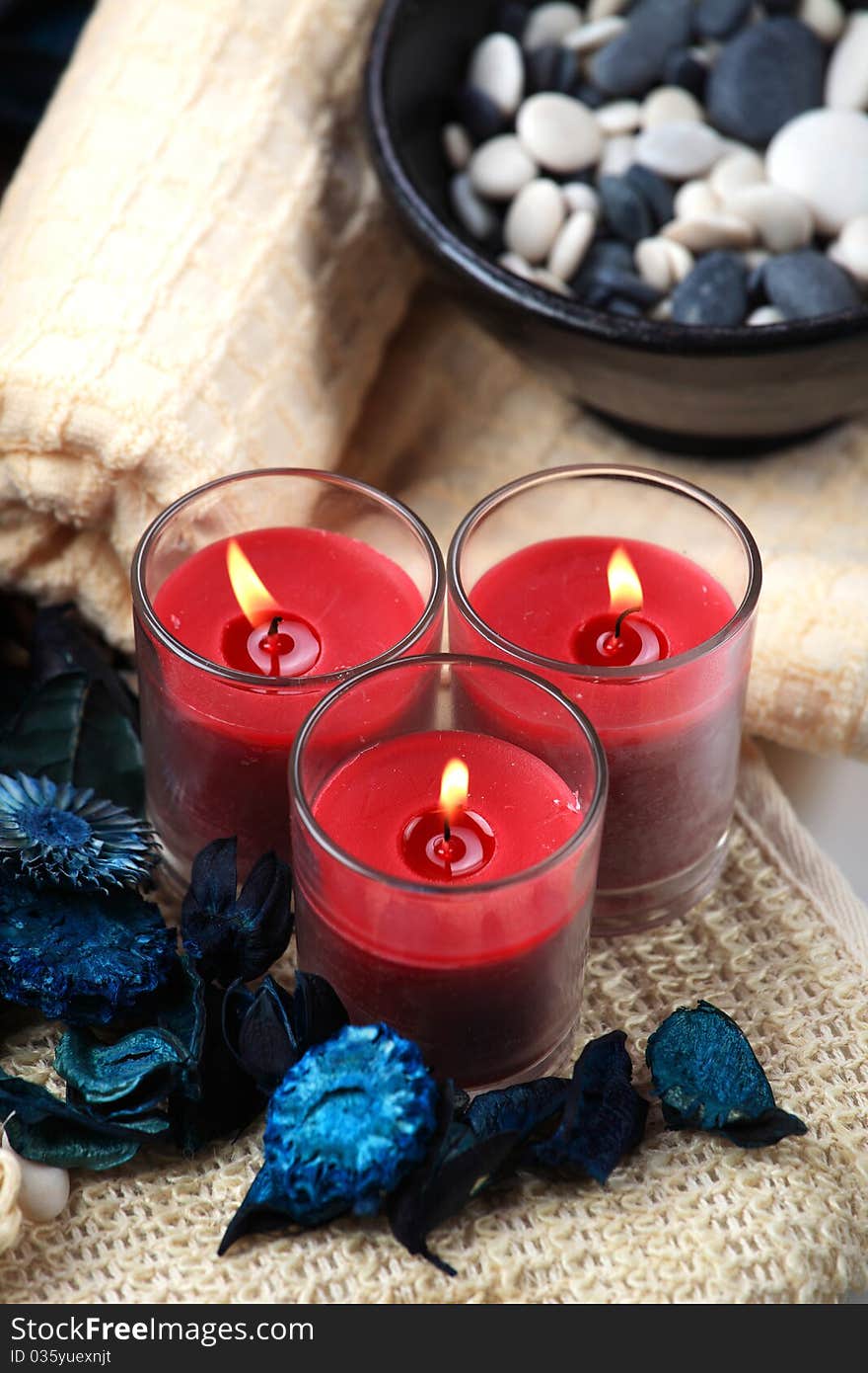 Three red candles and a bowl of black and white rocks on a towel