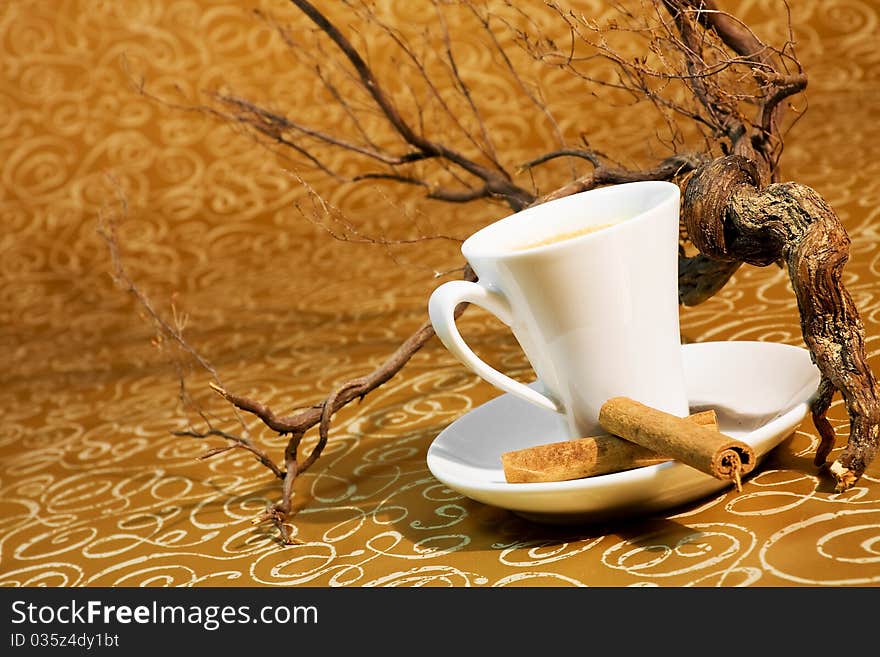 Cup of coffee with cinnamon sticks in the background with brown trunks