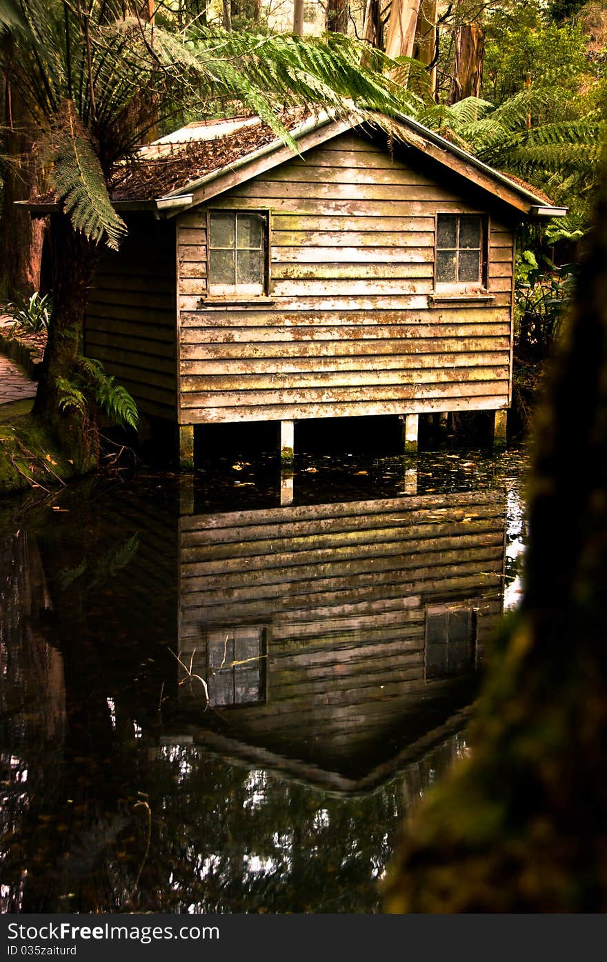 An old cabin and its reflection beside a pond in the middle of a forest.