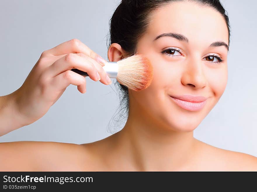 Beautiful woman applying make-up with brush