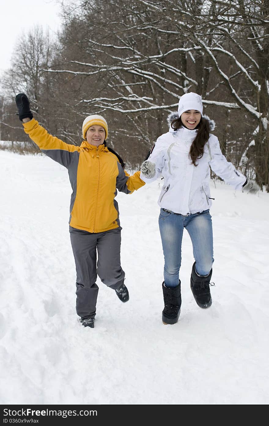 Two joyful women in winter jackets and caps run on