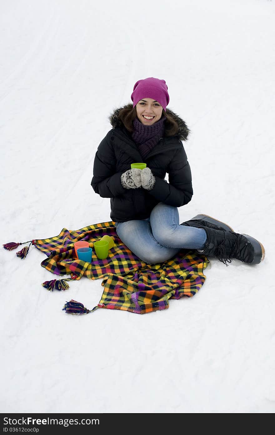 The young woman the brunette sits on a checkered plaid on snow with a mug