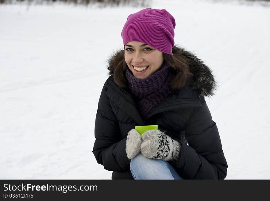 The young happy woman sits on snow with hands a cu