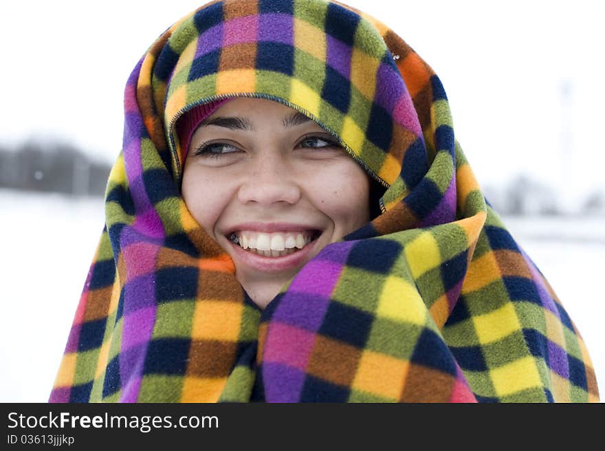 The young woman has muffled in a multi-colored plaid and smiles