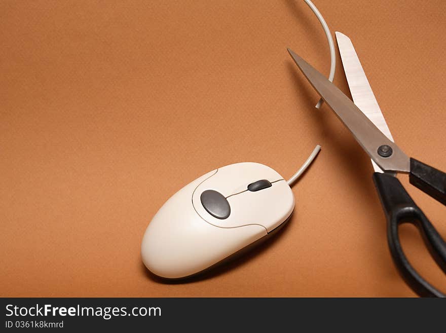 Scissors cutting cable of computer mouse on brown background. Scissors cutting cable of computer mouse on brown background