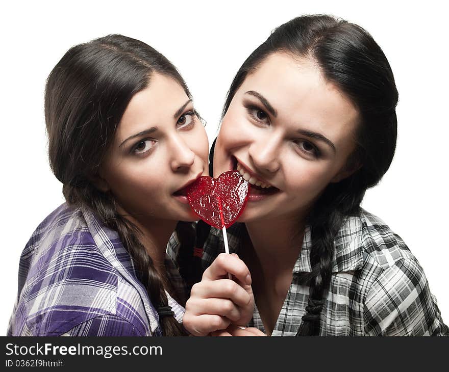 Two young smiling girl with red heart lolipop isolated on white