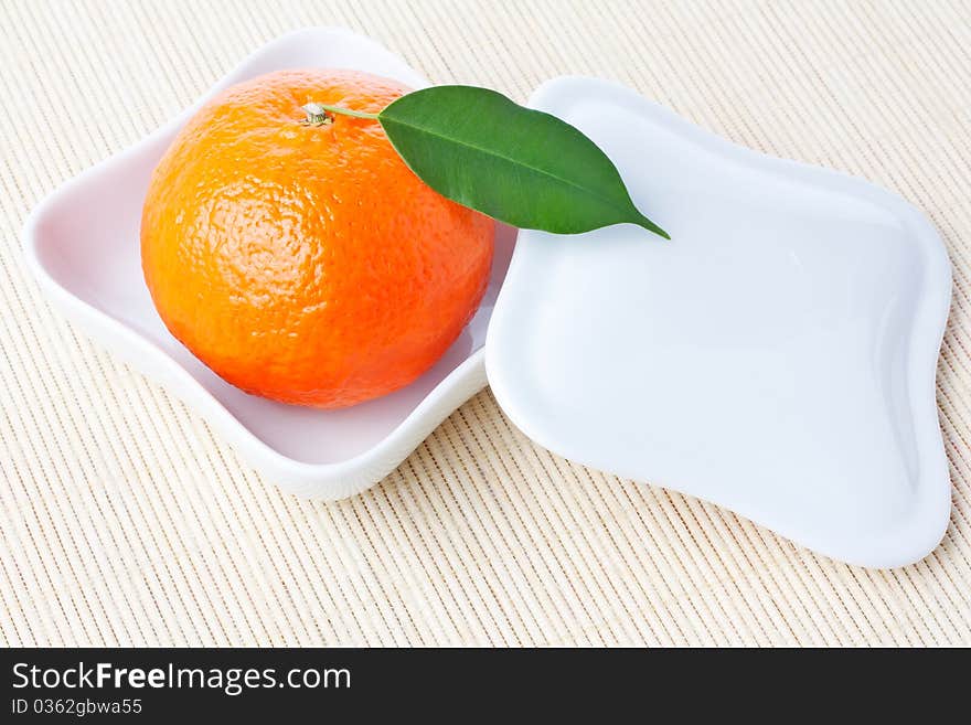 Ripe fresh orange tangerine with green leaf on white shaped plate with cover. Ripe fresh orange tangerine with green leaf on white shaped plate with cover