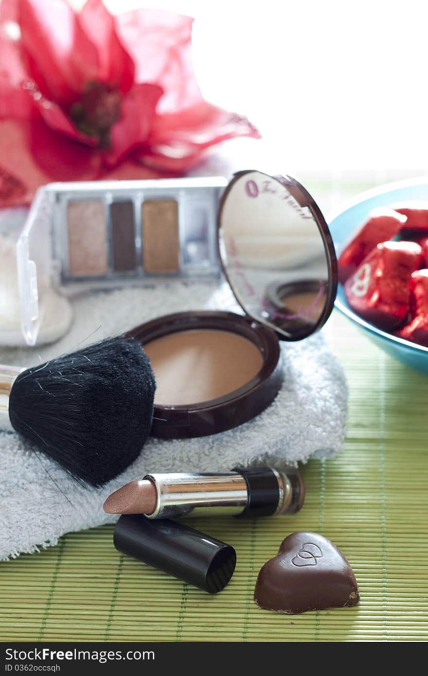 Various cosmetics and a heart-shaped chocolate resting on a bath-cloth. Various cosmetics and a heart-shaped chocolate resting on a bath-cloth