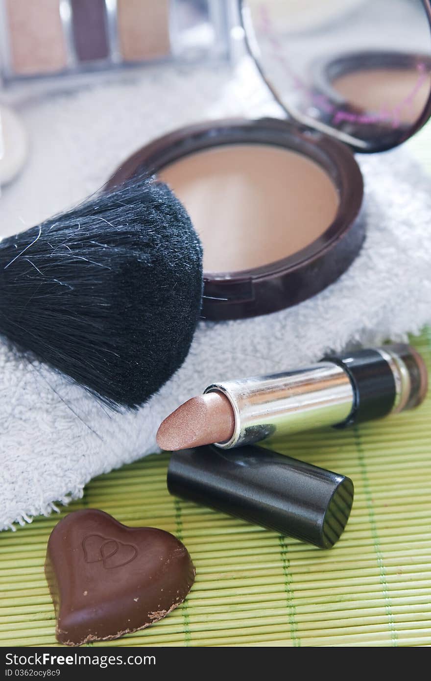 Various cosmetics and a heart-shaped chocolate resting on a bath-cloth. Various cosmetics and a heart-shaped chocolate resting on a bath-cloth