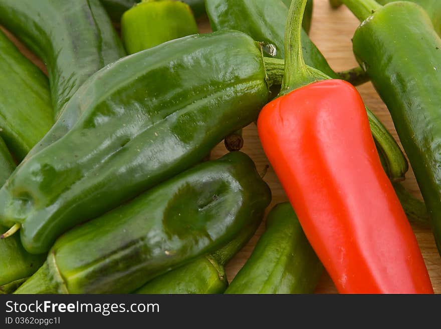 Close-up of green Spanish padron peppers and one red chilli pepper, wooden board background