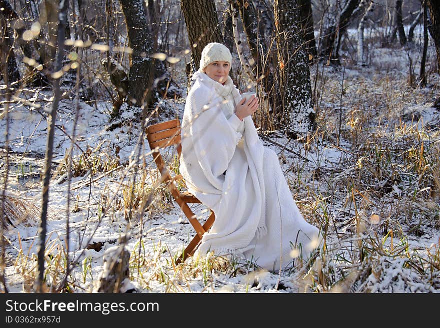 Woman in white, with a mug in his hands, wrapped in a blanket in a winter forest. sunset. Woman in white, with a mug in his hands, wrapped in a blanket in a winter forest. sunset.