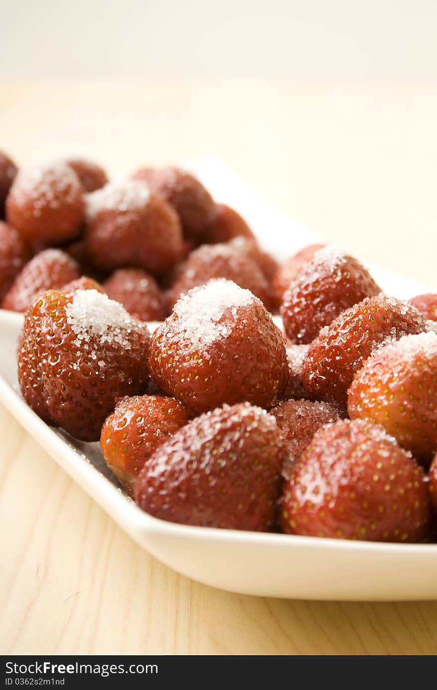 On the table is a plate of strawberries sprinkled with sugar. On the table is a plate of strawberries sprinkled with sugar