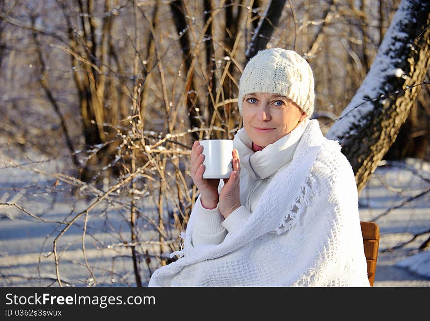 Woman in white, with a mug in his hands, wrapped in a blanket in a winter forest. Woman in white, with a mug in his hands, wrapped in a blanket in a winter forest.