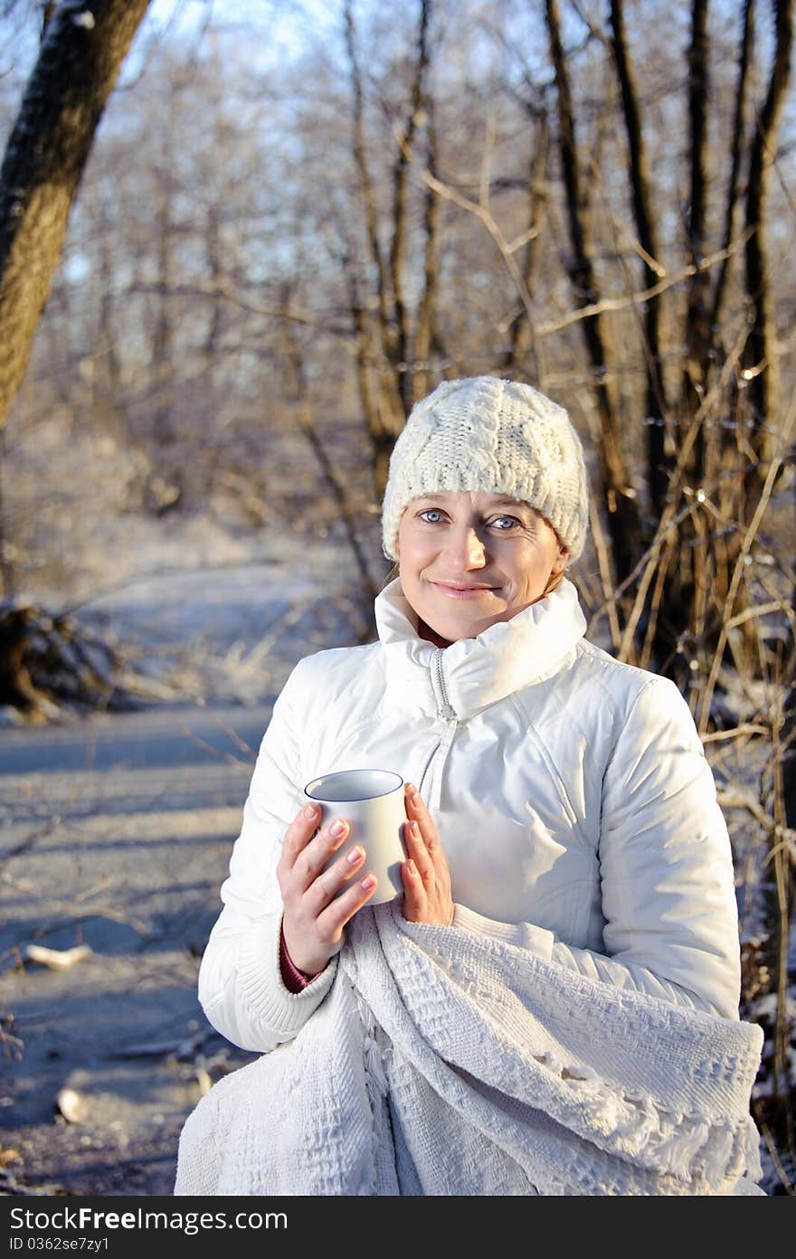 Woman in white, with a mug in his hands, wrapped in a blanket in a winter forest. Woman in white, with a mug in his hands, wrapped in a blanket in a winter forest.