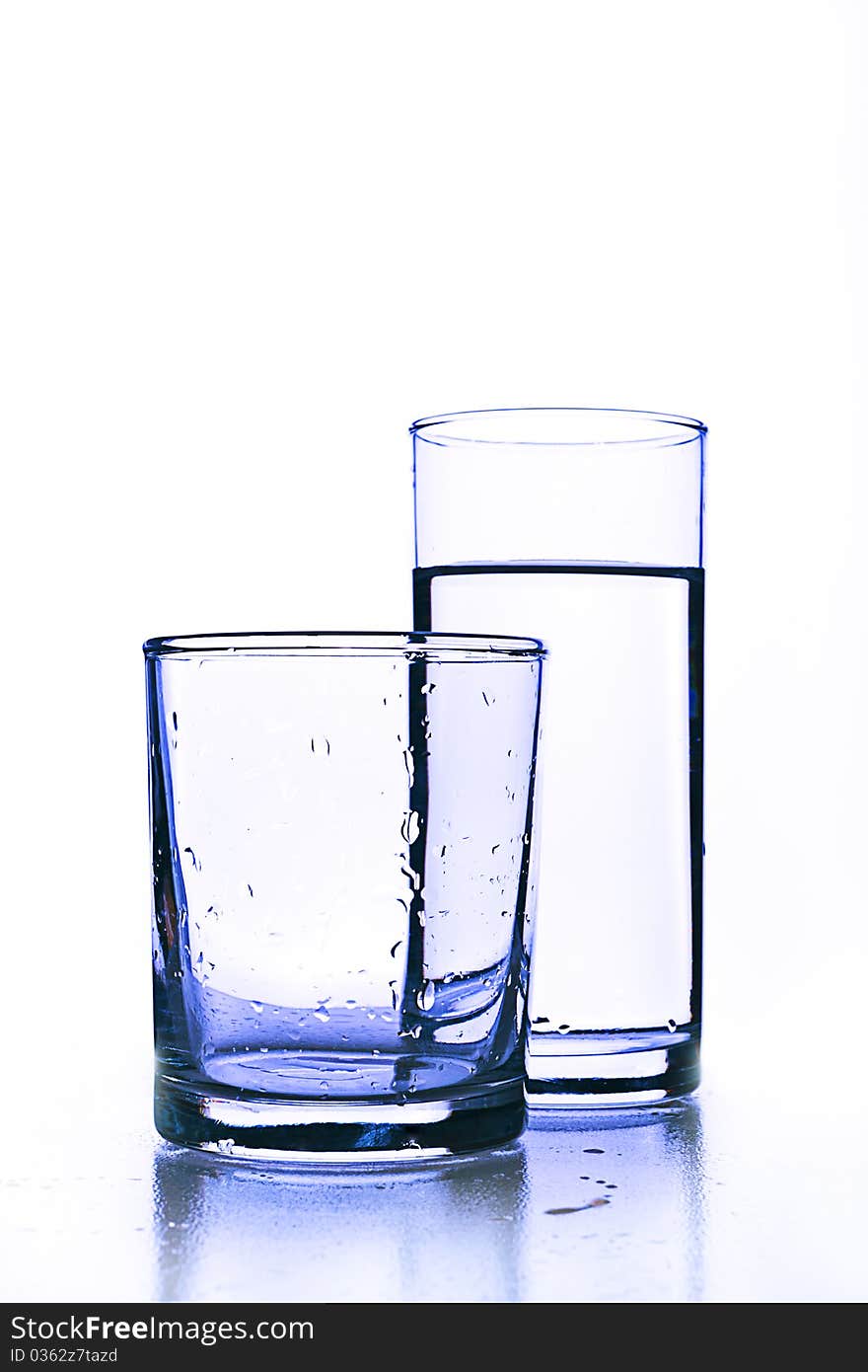 Empty glass with drops before full glass of clean water. Empty glass with drops before full glass of clean water