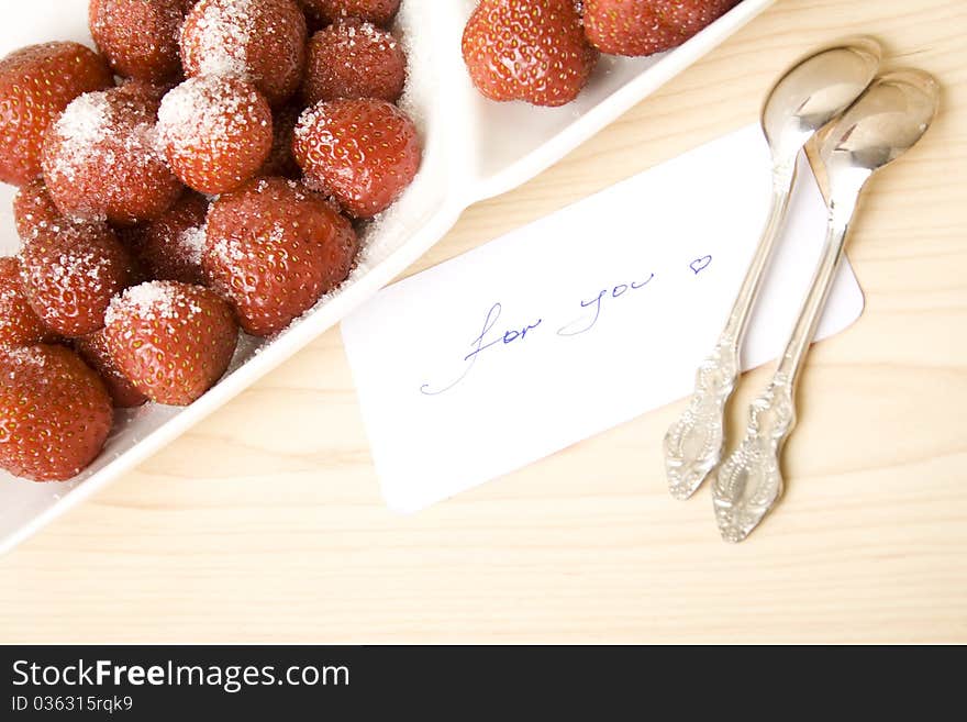 A plate of strawberries is on a wooden table. Nearby is a card with text for you. A plate of strawberries is on a wooden table. Nearby is a card with text for you