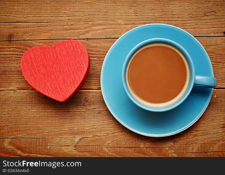 Cup of coffee and red box in heart shape on wood background