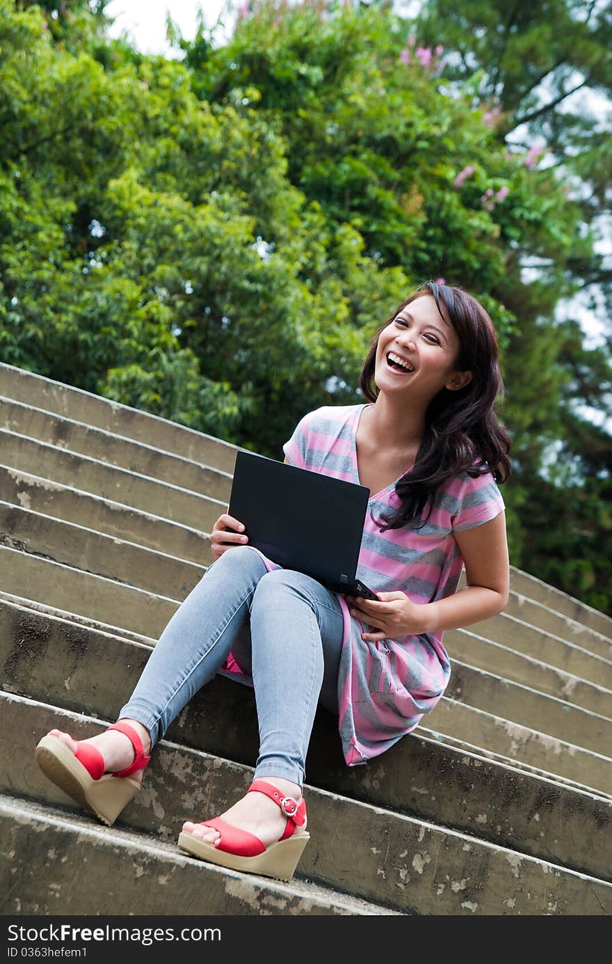 A happy female college student is working in university's park. A happy female college student is working in university's park