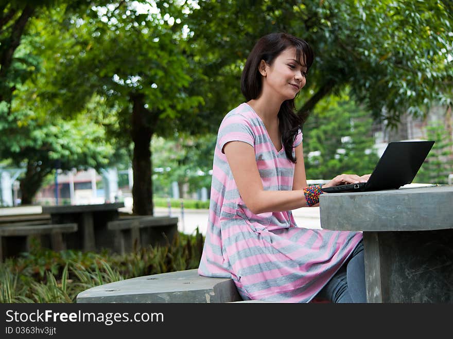 A happy female college student is working in university's park. A happy female college student is working in university's park