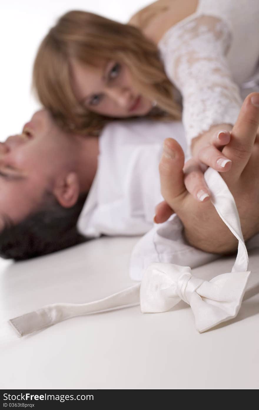 Romantic image of just married couple lying on the floor together. The groom holding a bow-tie (Focus on the bow-tie)