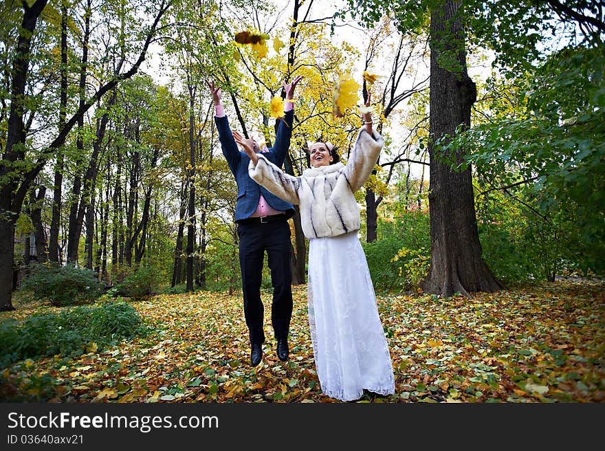 Joyful bride and groom throw the yellow leaves in autumn park