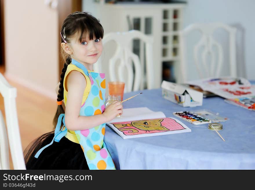 Adorable little girl with long dark hair draws in the kitchen