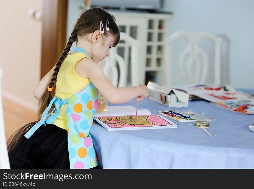 Adorable little girl with long dark hair draws in the kitchen